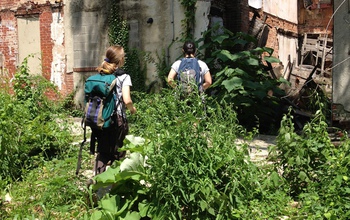 Two women researchers look for mosquito habitat and larvae near an abandoned building.